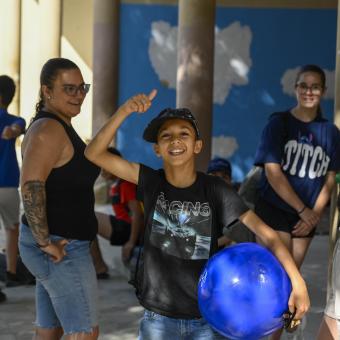 Un niño beneficiario del programa CaixaProinfancia sonríe a cámara sujetando una pelota. 