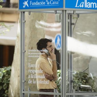 Un chico joven escuchando el testimonio de una persona mayor desde la cabina telefónica. 