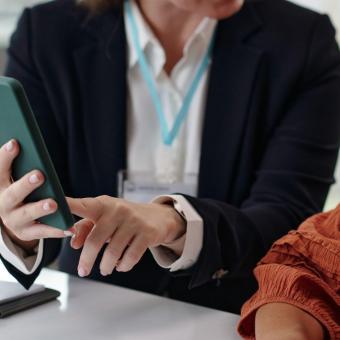 Dos mujeres hablando, una señala la pantalla de un teléfono inteligente.