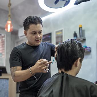 Juan Gabriel Agudelo cortándole el pelo a uno de sus clientes. 