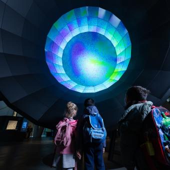 Unos niños y niñas observan el módulo sobre el Big Bang en CosmoCaixa.