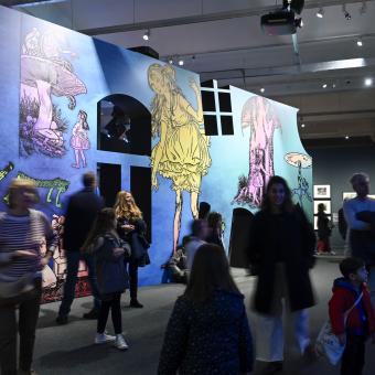 Visitors in front of a reproduction of Lola Anglada's illustrations at the exhibition «The Worlds of Alice. Dreaming of Wonderland».