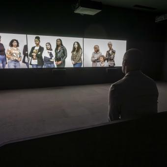 Visitante delante de la videoinstalación de tres canales de la exposición «Fuera de marco. Obras de Rineke Dijkstra y Philippe Parreno».