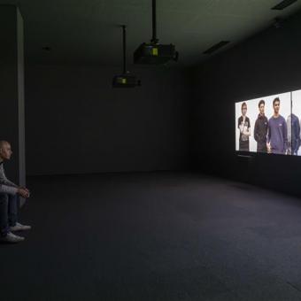 Visitante delante de la videoinstalación de tres canales de la exposición «Fuera de marco. Obras de Rineke Dijkstra y Philippe Parreno».