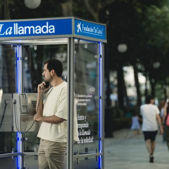 Un chico joven escuchando el testimonio de una persona mayor desde la cabina telefónica en Granada. 