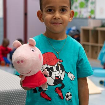 Un niño beneficiario del programa CaixaProinfancia sonríe a cámara con su peluche en la mano.