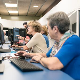 Personas mayores siguiendo las instrucciones de una docente en sus ordenadores.