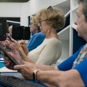 Personas mayores siguiendo las instrucciones de una docente en sus teléfonos móviles.