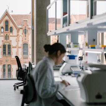Una investigadora en los laboratorios del CaixaResearch Institute. Al fondo, el edificio del Museo de la Ciencia CosmoCaixa.