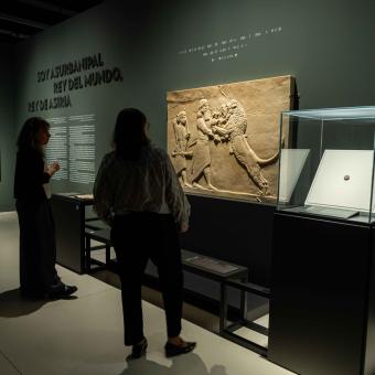 Two visitors admiring one of the pieces on display at the "Ashurbanipal" exhibition at CaixaForum Madrid.
