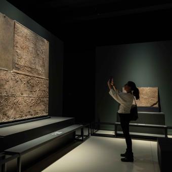 A visitor taking a photo of one of the pieces in the "Ashurbanipal" exhibition at CaixaForum Madrid.