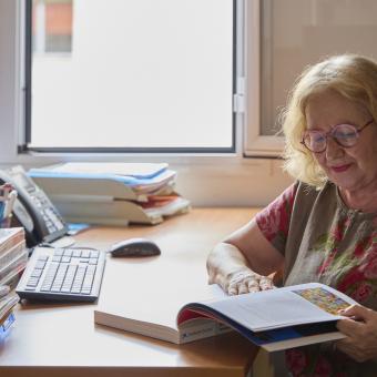 Persona mayor en un escritorio ojeando un libro.