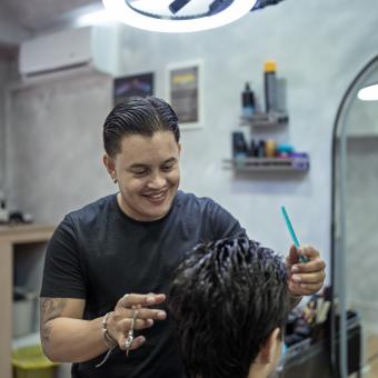 Juan interactuando con uno de sus clientes mientras le hace un corte de pelo. 