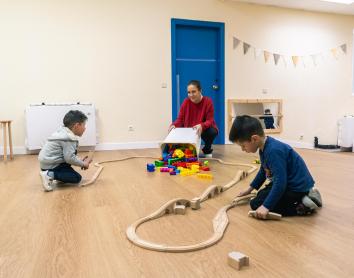 Dos nens i una tècnica juguen amb un circuit de cotxes de joguina als Espais de Creixement 3-6 de CaixaProinfància a l'Associació Barró.