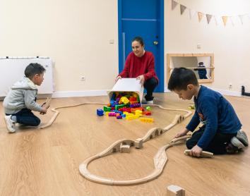 Dos niños y una técnica juegan con un circuito de coches de juguete en los Espacios de Crecimiento 3-6 de CaixaProinfancia en la Asociación Barró. 