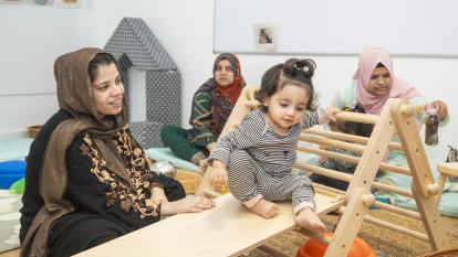 A mother looks at her daughter, playing on a Pikler learning structure.