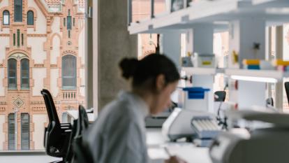 Una investigadora en los laboratorios del CaixaResearch Institute. Al fondo, el edificio del Museo de la Ciencia CosmoCaixa.