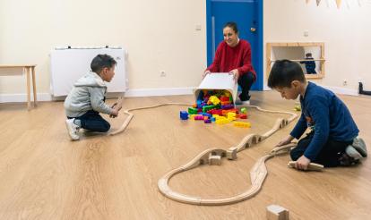 Dos nens i una tècnica juguen amb un circuit de cotxes de joguina als Espais de Creixement 3-6 de CaixaProinfància a l'Associació Barró.