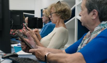 Personas mayores siguiendo las instrucciones de una docente en sus teléfonos móviles.