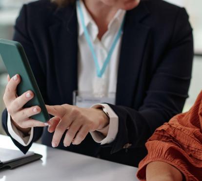 Dos mujeres hablando, una señala la pantalla de un teléfono inteligente.
