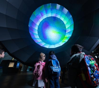 Unos niños y niñas observan el módulo sobre el Big Bang en CosmoCaixa.