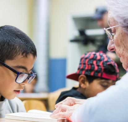 Persona mayor voluntaria ayuda a un niño en sus estudios.