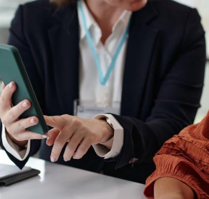Dos mujeres hablando, una señala la pantalla de un teléfono inteligente.