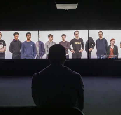 Visitor in front of the three-channel video installation of the exhibition Out of Frame. Works by Rineke Dijkstra and Philippe Parreno.