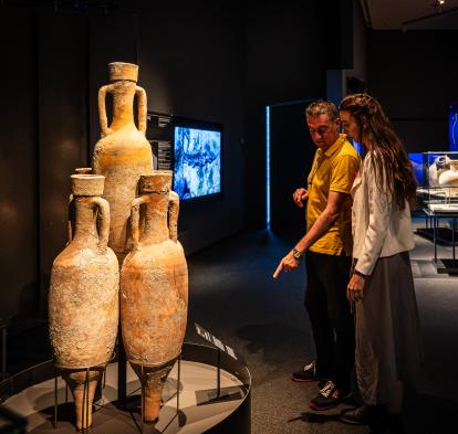 Dos personas observando algunas de las piezas presentes en la muestra «Naufragios. Arqueología sumergida» en CaixaForum Zaragoza. 