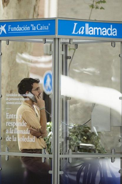 Un chico joven escuchando el testimonio de una persona mayor desde la cabina telefónica.
