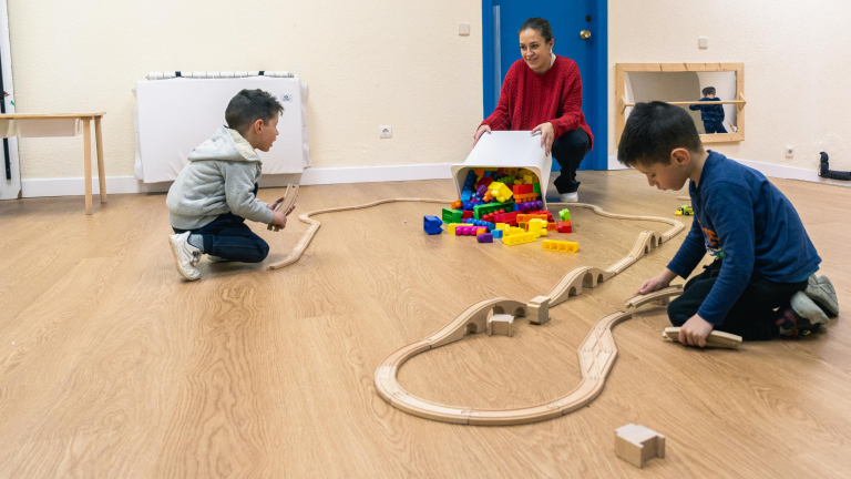 Two children and a teacher play with a toy car track in the CaixaProinfancia 3-6 Growth Spaces at the Barró Association.