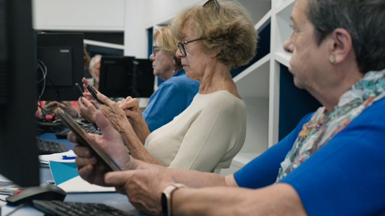 Personas mayores siguiendo las instrucciones de una docente en sus teléfonos móviles.